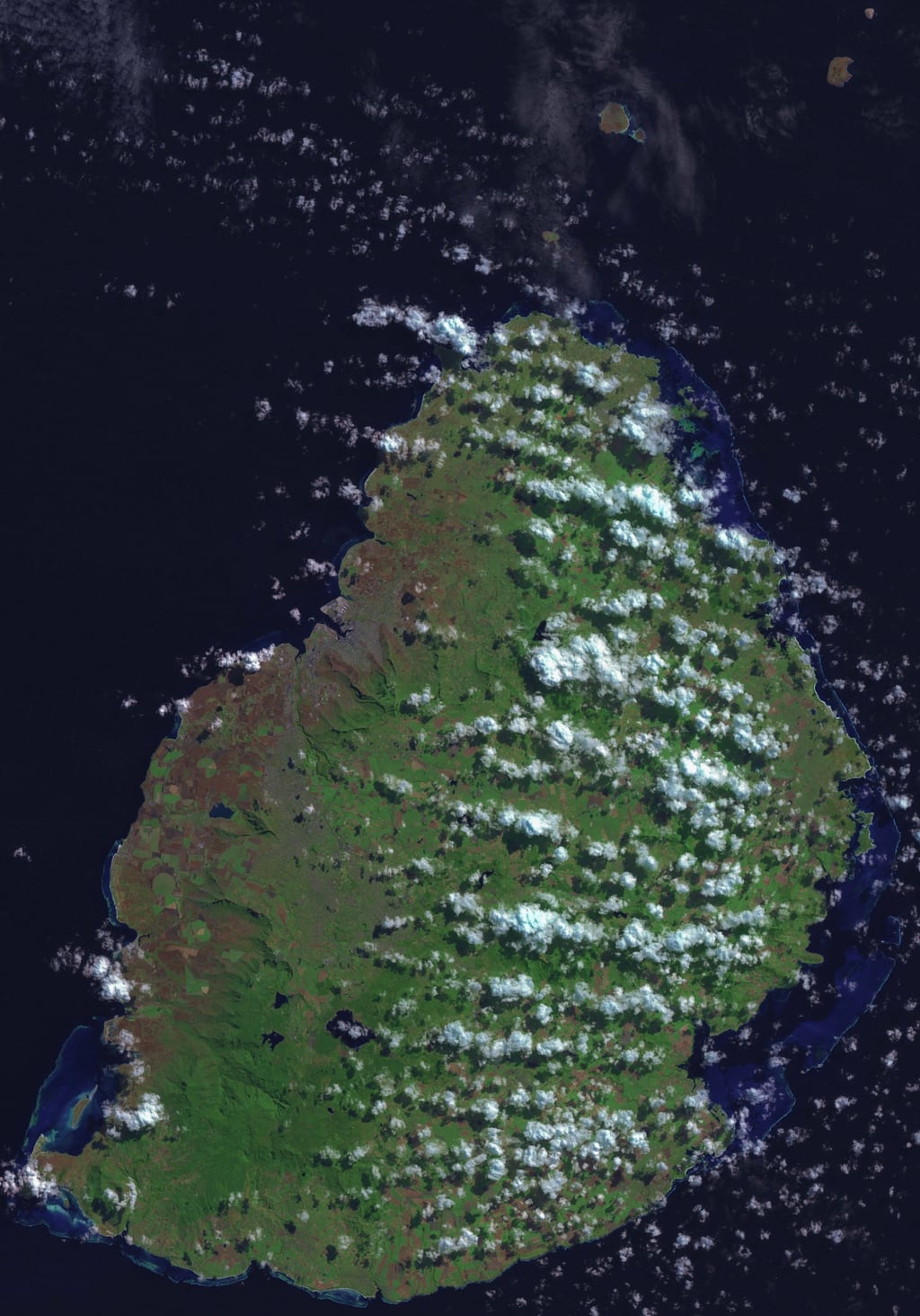Real public-domain NASA satellite image of the island of Mauritius, viewed from above. The island fills most of the frame, surrounded by deep navy ocean. The mountainous green interior, paler coastal plains, and turquoise lagoon along the coast are clearly visible. Some natural cloud cover crosses the island. Used as a service-area illustration; no roads or place names overlaid.